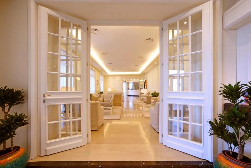 Ingresso della hall con porte a vetri bianche, salotti chiari e piante decorative