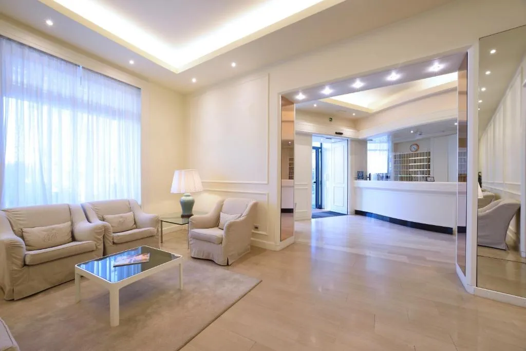 Hall con salotto dai divani beige, reception sullo sfondo e ampie finestre luminose