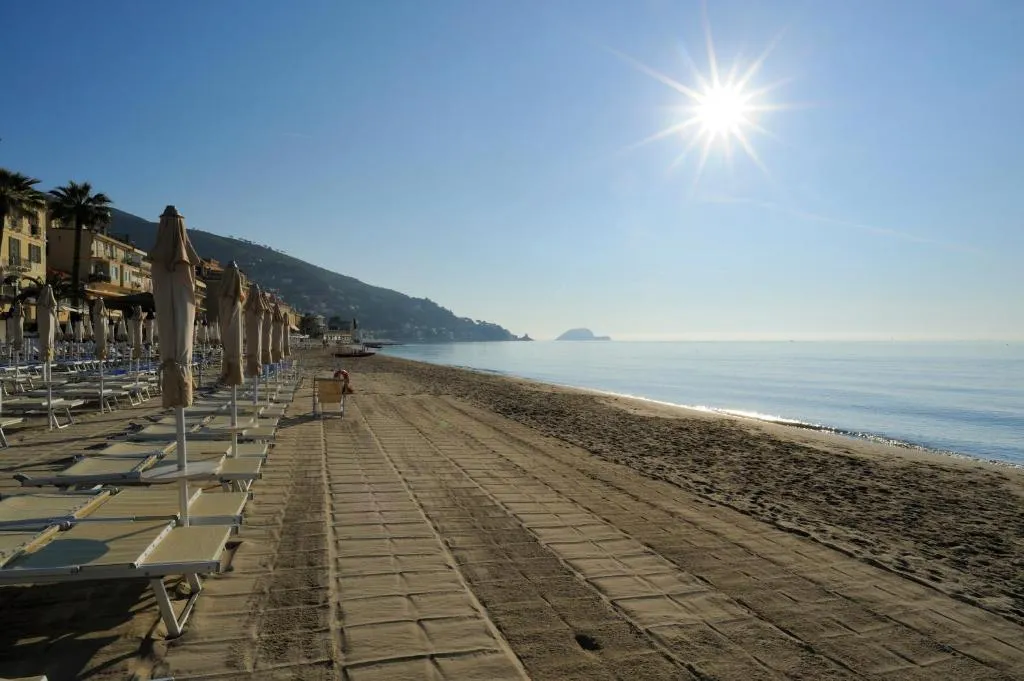 Lunga spiaggia sabbiosa con lettini, palme e promontorio sullo sfondo in una giornata di sole
