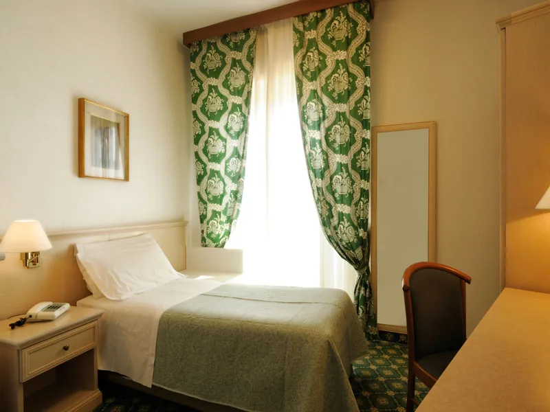 Camera singola con letto, tende verdi decorate e arredi in legno