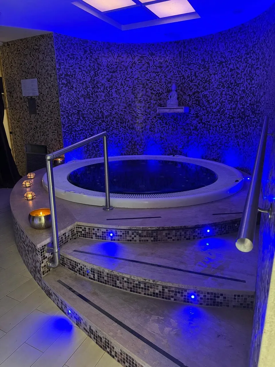 Vasca idromassaggio circolare con luci blu, candele e statua di Buddha nella spa
