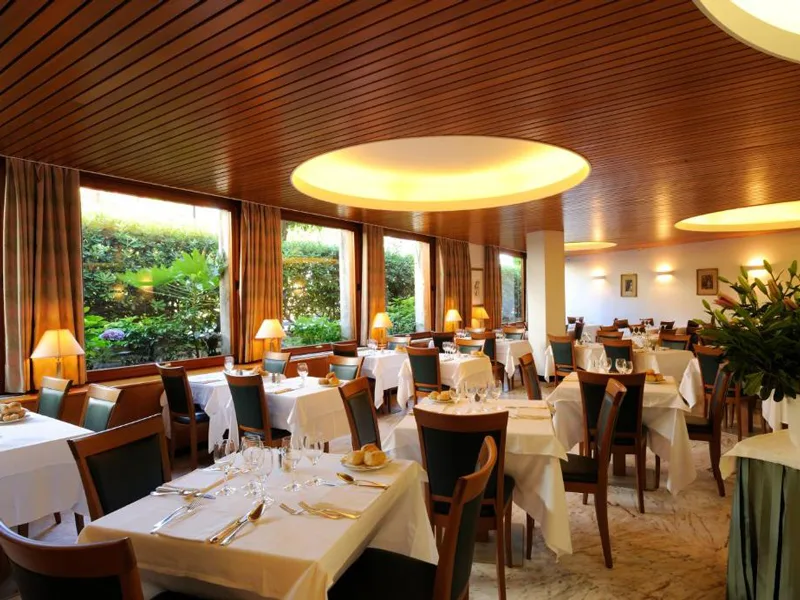 Sala ristorante elegante con tavoli apparecchiati, soffitto in legno e finestre sul giardino